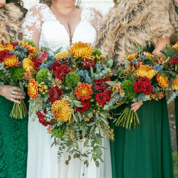 fall-featured Up close view of a bride and her bridesmaids in green with orange, yellow, and red bouquets for a fall wedding