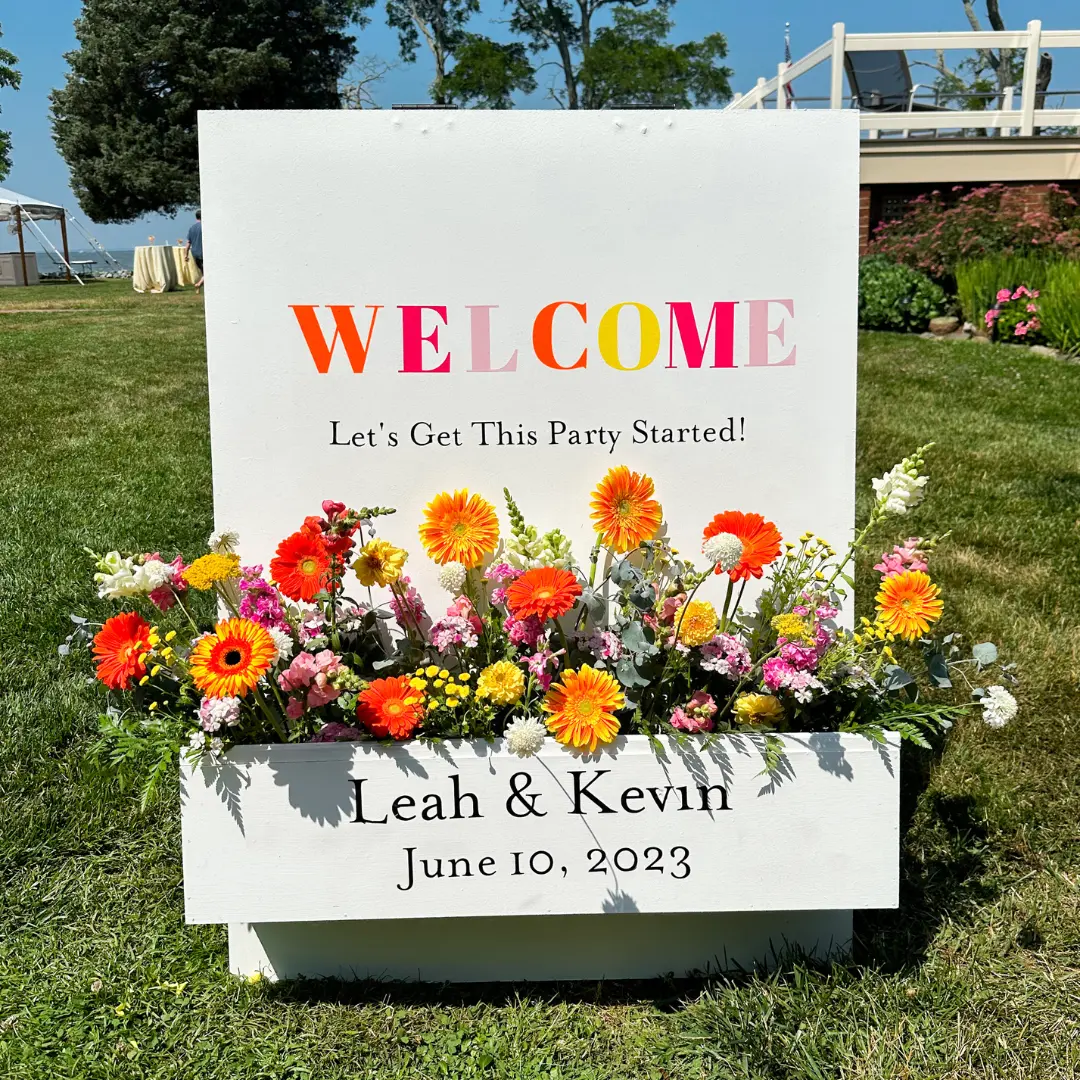 summer A welcome flower box sign with orange and yellow accents at a wedding