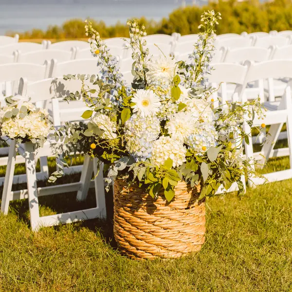 Blue and white florals in a wicker basket at the end of a chair row for a ceremony