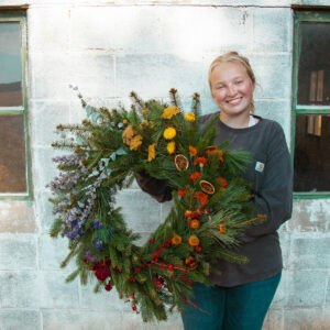 Woman holds a large Christmas Wreath with rainbow color floral additions.