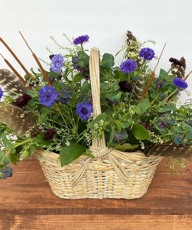 Sympathy Basket Arrangement with blue flowers and feathers.