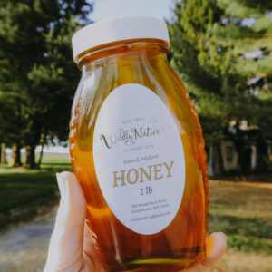 Hand Holding a jar of floral honey up to the sunlight