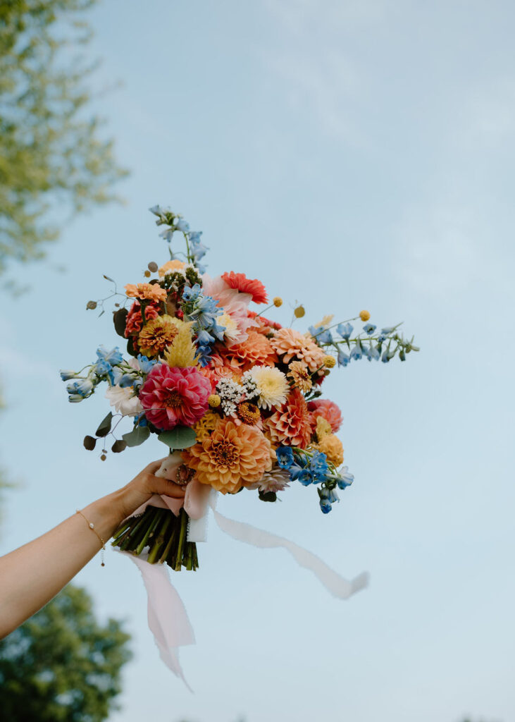 Colorful pastel bridal bouquet is held up against a blue sky.