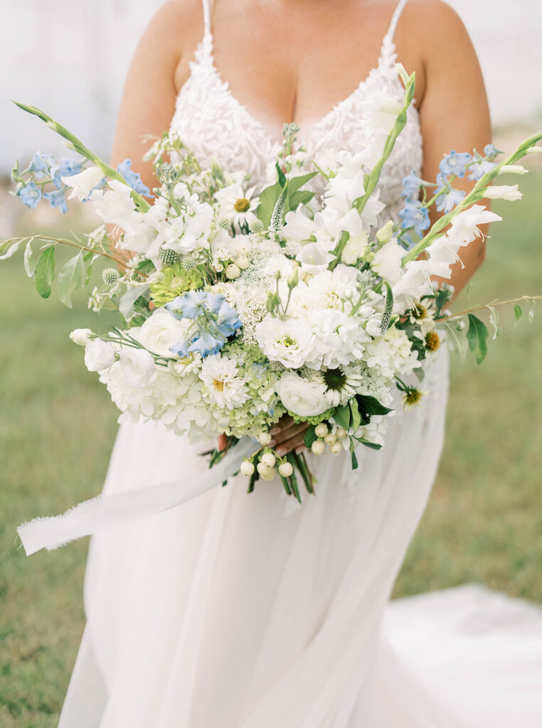 Bride holds a blue and white bouquet in front of her dress.