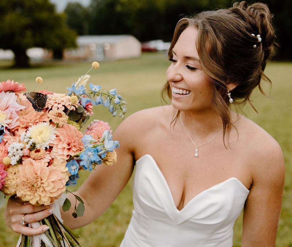 Bride looks at bouquet with butterfly perched on top.