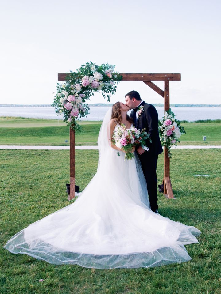 pink and white flowers on arch with bride and groom underneath