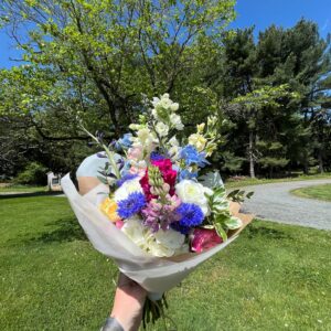 Hand holds a bouquet of cut flowers wrapped in paper up to the blue sky.