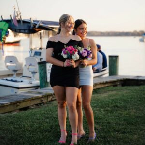 Two women stand next to each other holding floral bouquets dressed for a high school dance.
