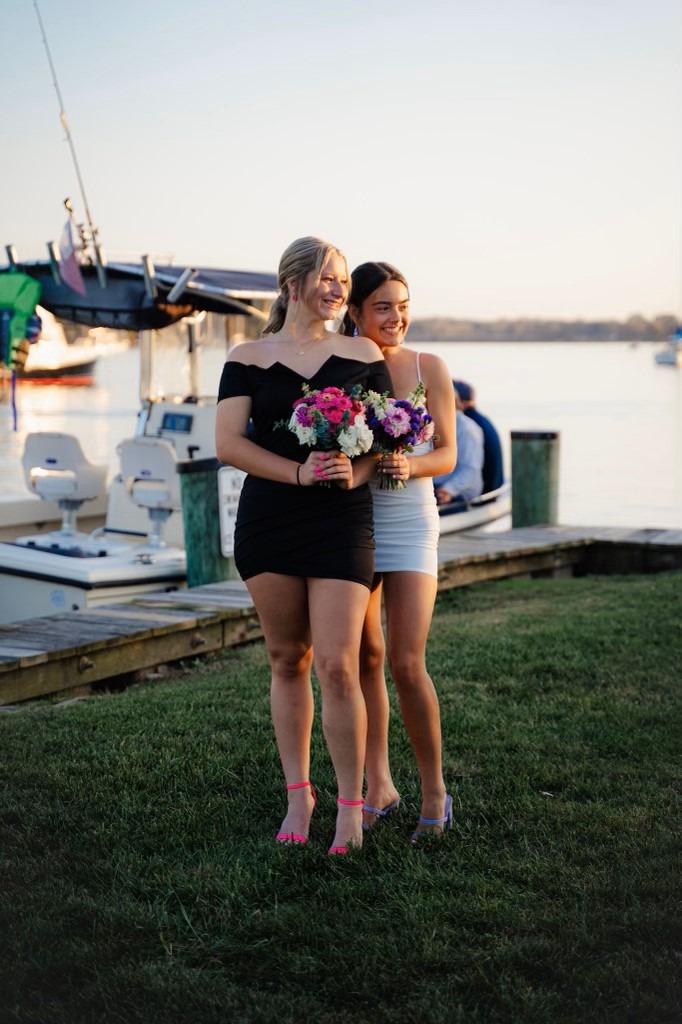 Two women stand next to each other holding floral bouquets dressed for a high school dance.
