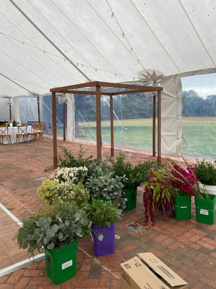 Wooden Chuppah on a brick patio with buckets of fresh flower farm florals ready to be used.