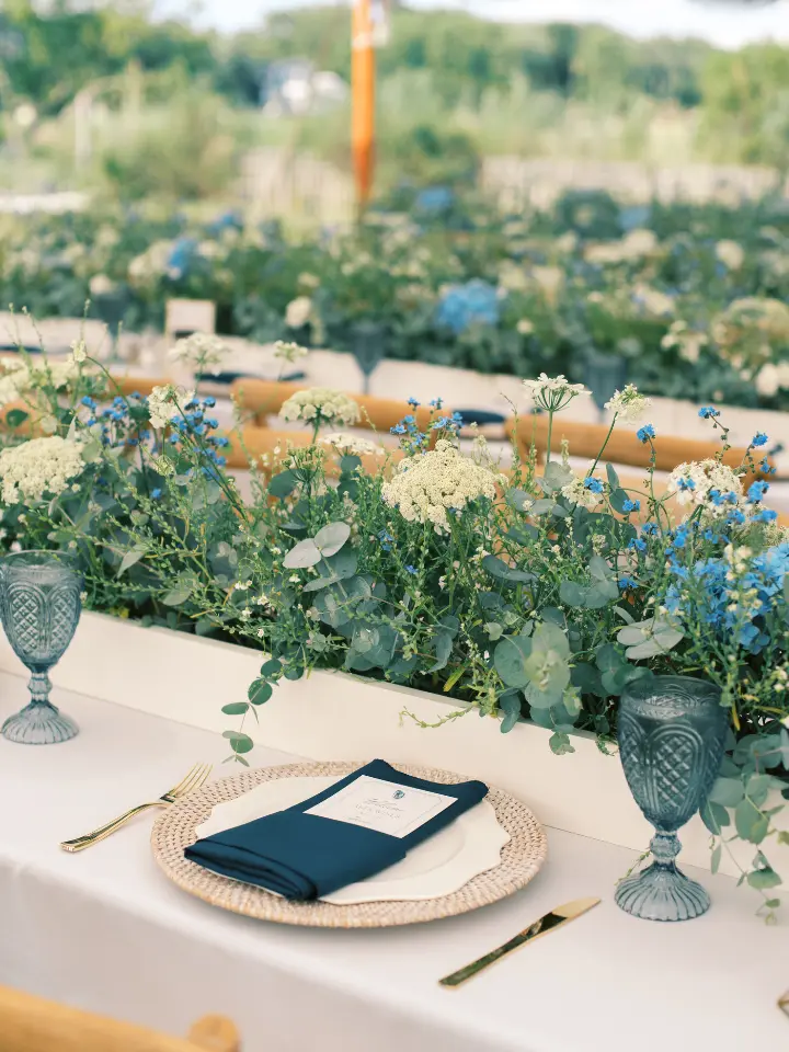 weddingtable Long rectangle table with tan linen, beige charger and blue napkin with a greenery long arrangement