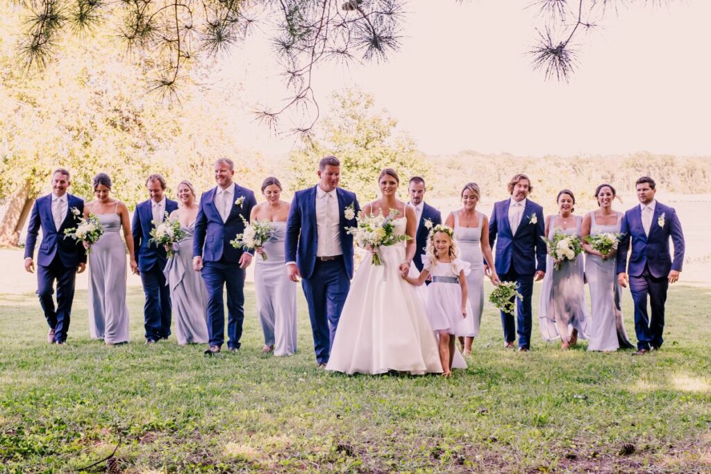 Full wedding party stands in a line with bride and groom in middle.