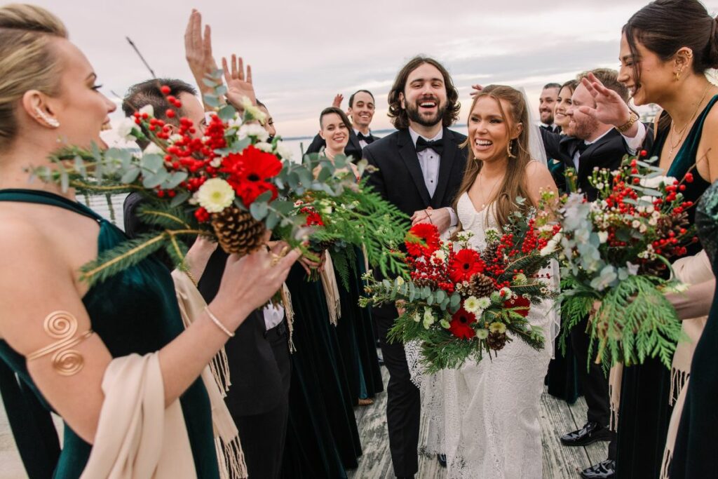 Bride and Groom carry their wedding flowers down an aisle created by their smiling wedding party.