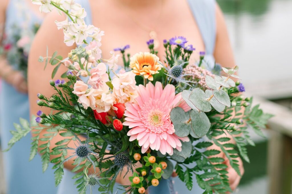 A bridesmaid in blue dress holds her pastel spring wedding bouquet for a closeup.