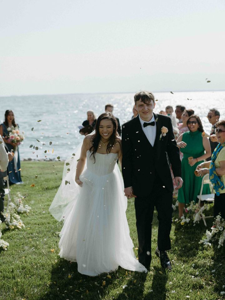 Bride and Groom walk back down the aisle while guests toss petals in the air.