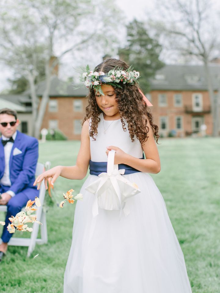 Flower girl tosses petals down the aisle with a flower crown in her hair.