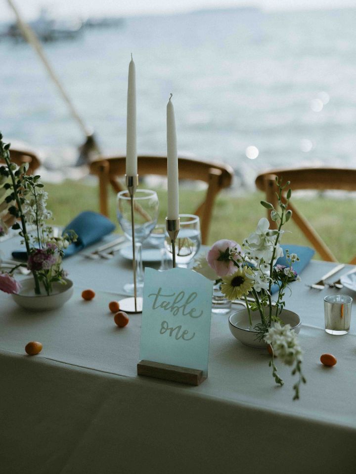 Wedding reception table with white tablecloth, blue napkins, gold candlesticks, and floral frog dishes.