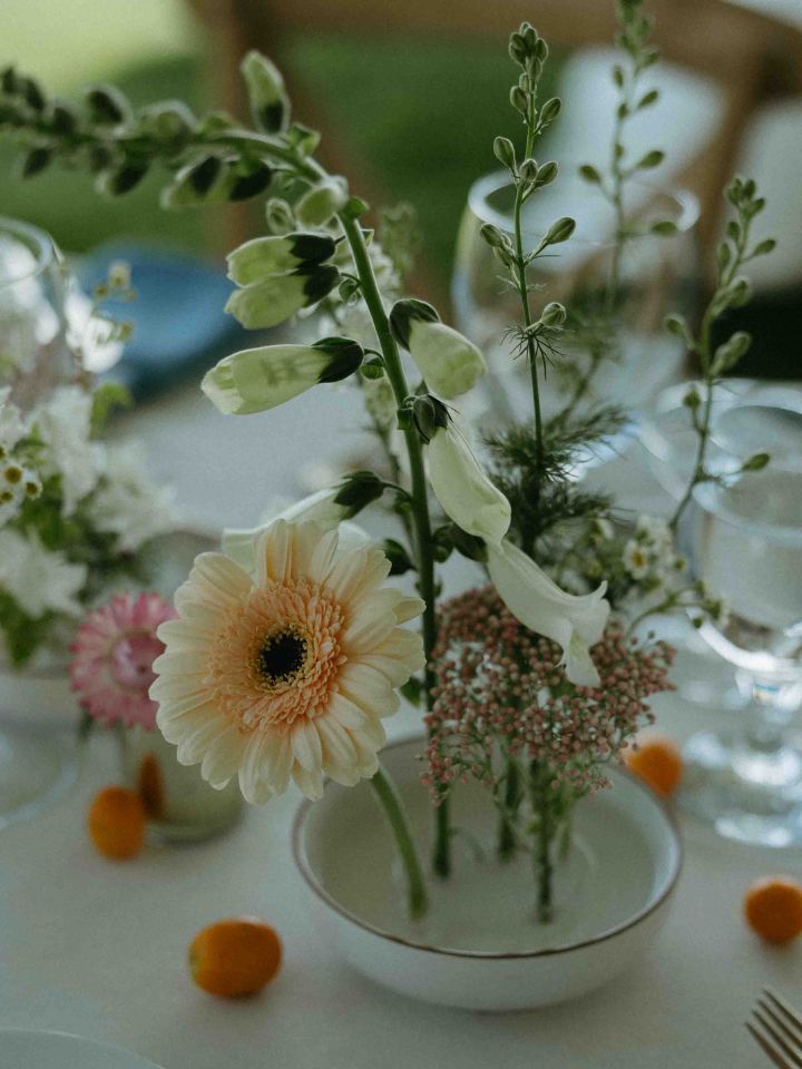 Wedding reception table with white tablecloth, blue napkins, gold candlesticks, and floral frog dishes.