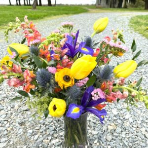 A bright and colorful Mother's Day Vase flower arrangement sits outdoors on a gravel driveway.