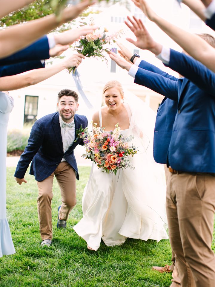 Bride and Groom go through a tunnel of their wedding party with arms raised.