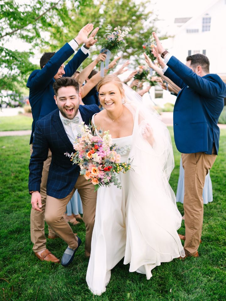 Bride and Groom go through a tunnel of their wedding party with arms raised.