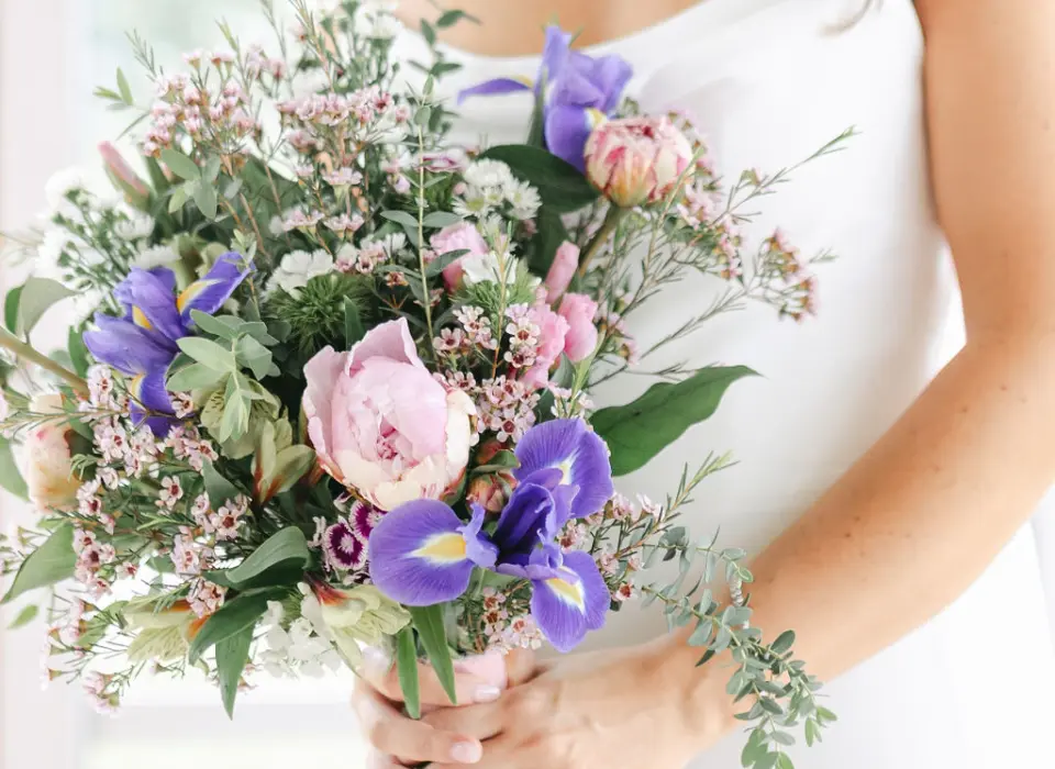 Up close of a bridal in a white gown holding a bouquet of light pink and lavendar and purple flowers