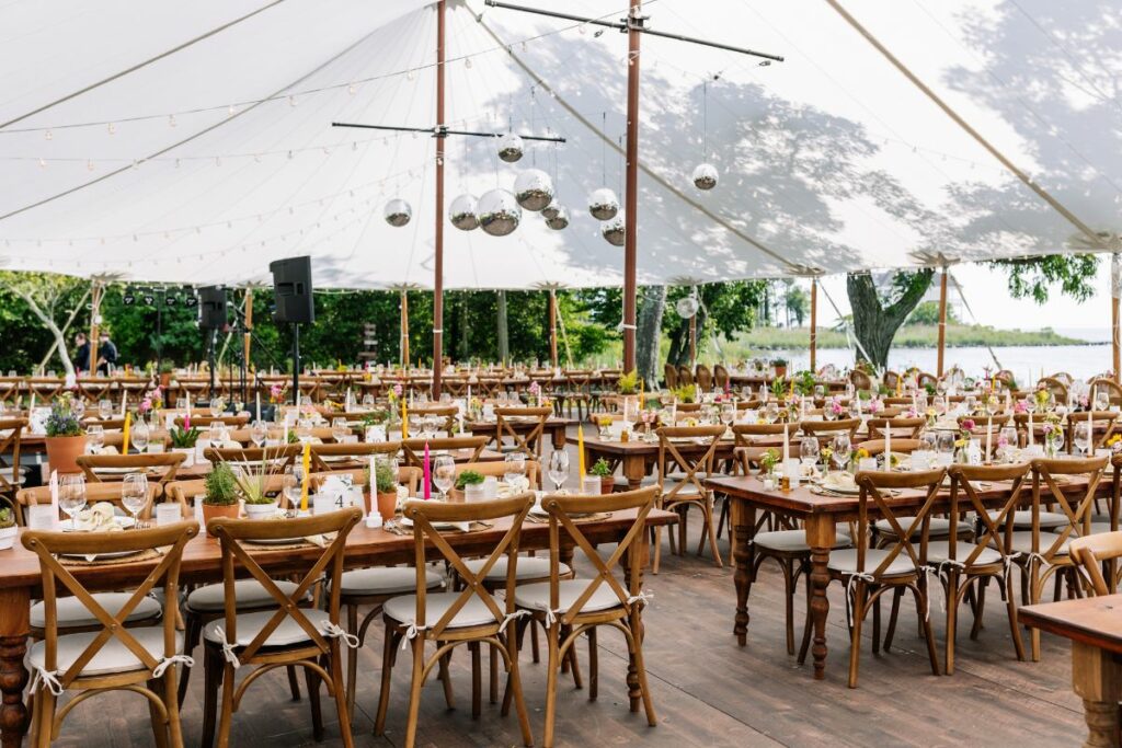 View of a sailcloth tent with flooring, disco install, and harvest farm tables.