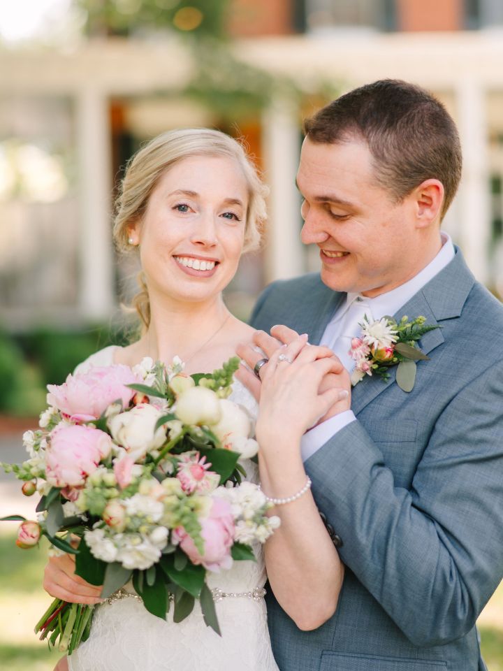 Bride and groom smile holding hands under a pergola for an outdoor wedding ceremony.