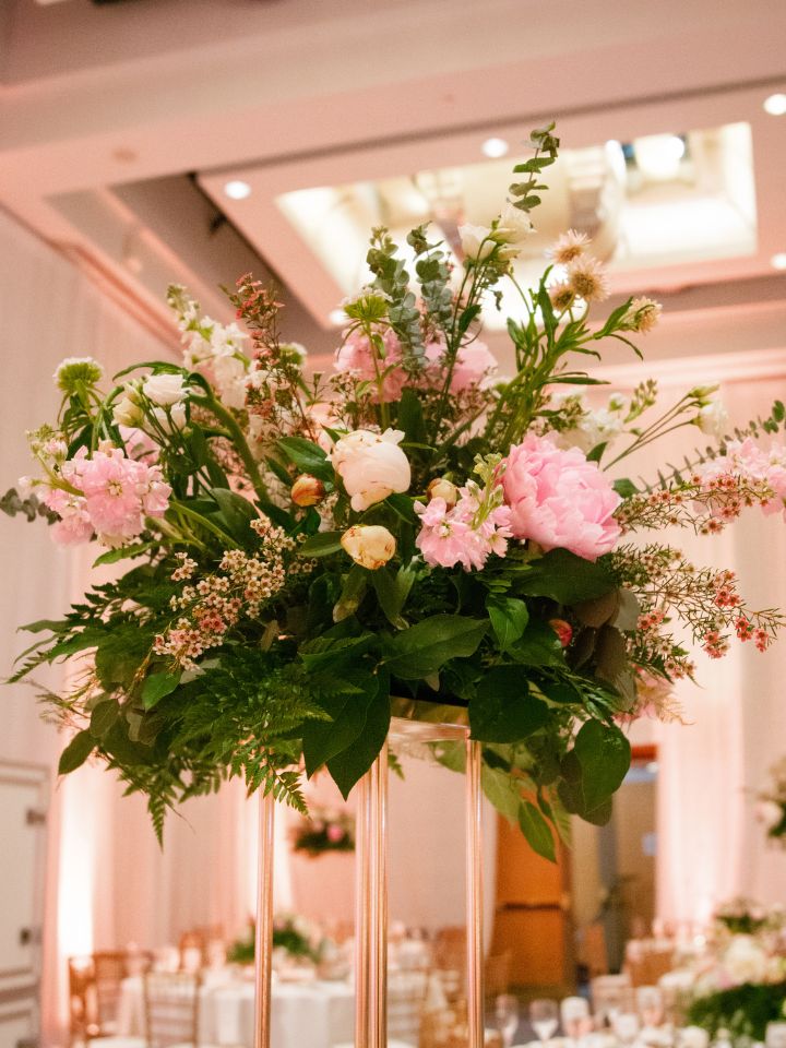 Gold pedestal holds up a floral arrangement on a wedding reception table.