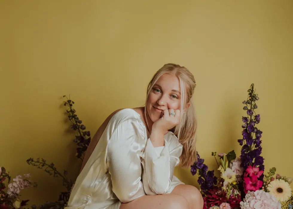 povafterweddingblues_featuredimage Lizzie, Wildly Native Flower Farm's floral designer, smiling at the camera while crouching against a yellow background with florals