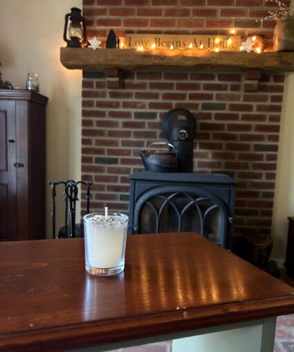 Votive candle on a table in front of a fireplace.