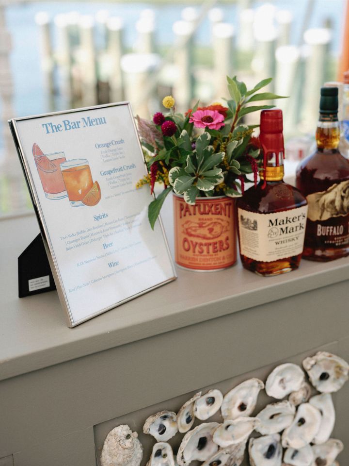A small vintage oyster tin full of summer wedding flowers sits on a bartop.