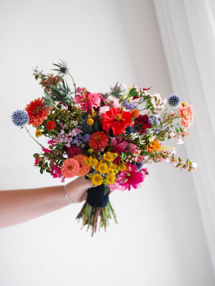 Bright and wild summer wildflower bridal bouquet is held up against a white background.