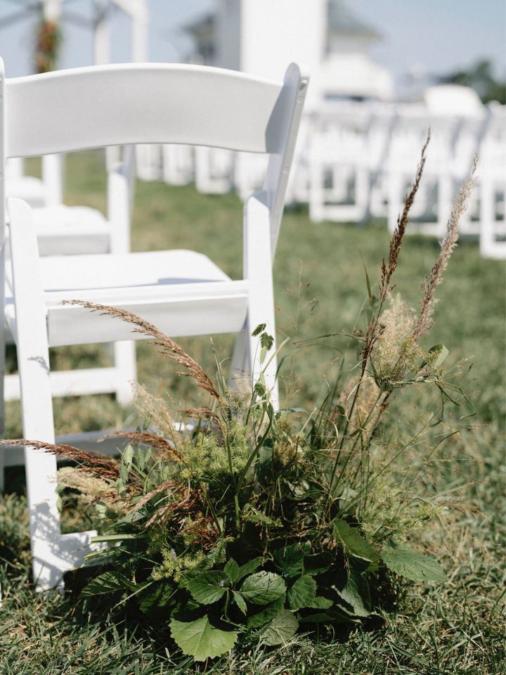 A low arrangement of local and native grasses marks the entrance to the wedding ceremony aisle at an outdoor wedding.