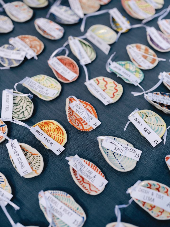 Closeup of brightly colored ceramic escort cards in the shape of oyster shells on a blue table linen.