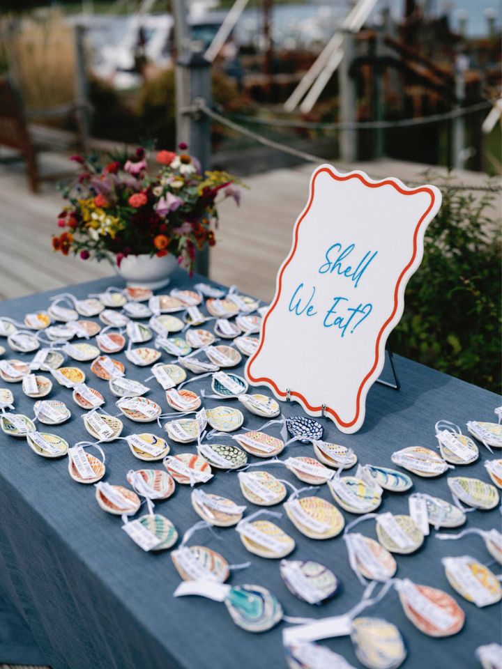 Escort card table at a wedding with a white porcelain compote with a summer flower arrangement.