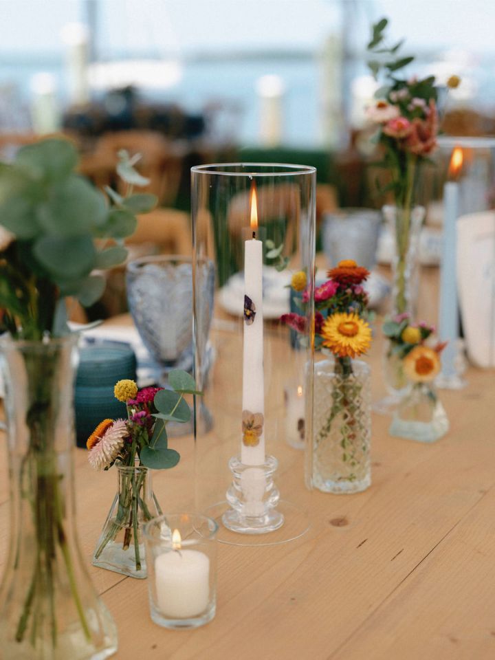Taper candle with Wildly Native pressed flowers on a table with bud vases.