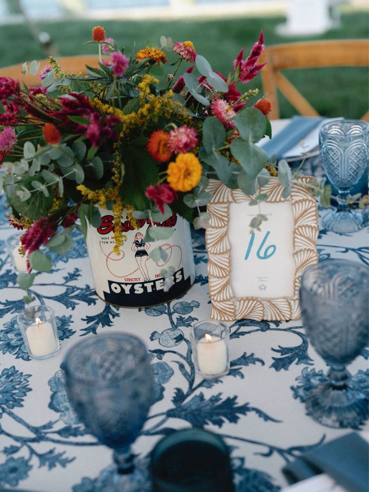 Blue and white patterned linen on a guest table in a wedding reception with vintage oyster tin and floral centerpiece.