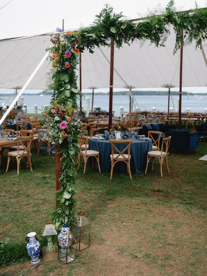 A greenery garland with floral accents wraps the entrance to the sailcloth tent for a waterfront wedding reception.