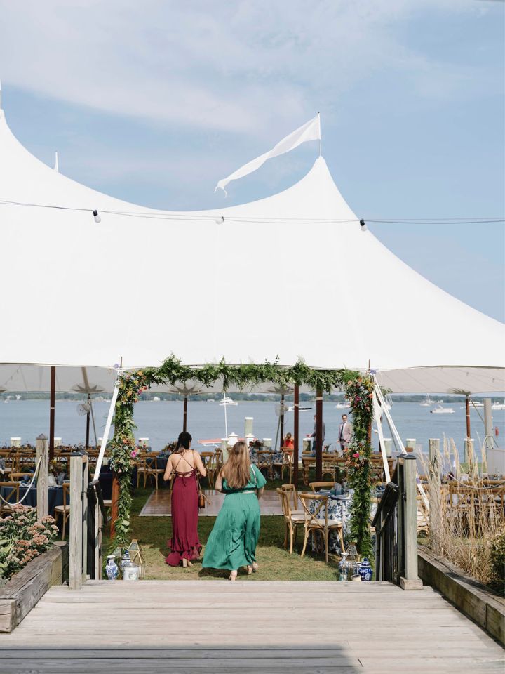 A white sailcloth tent under a clear blue sky welcomes wedding guests to the reception.