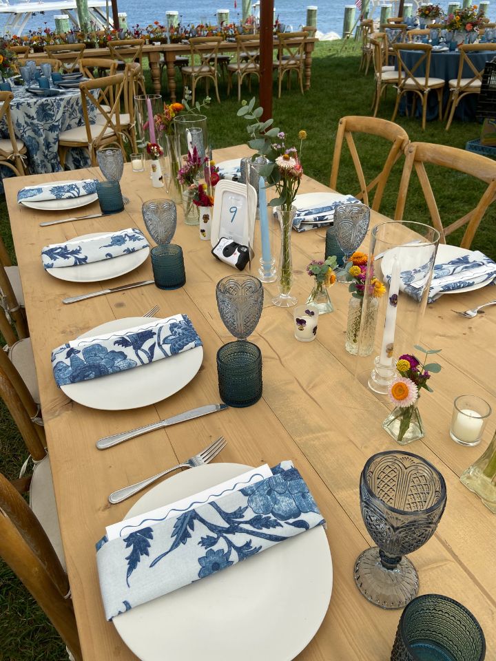 Light wood harvest table with scattered bud vases, taper candles, and votives.
