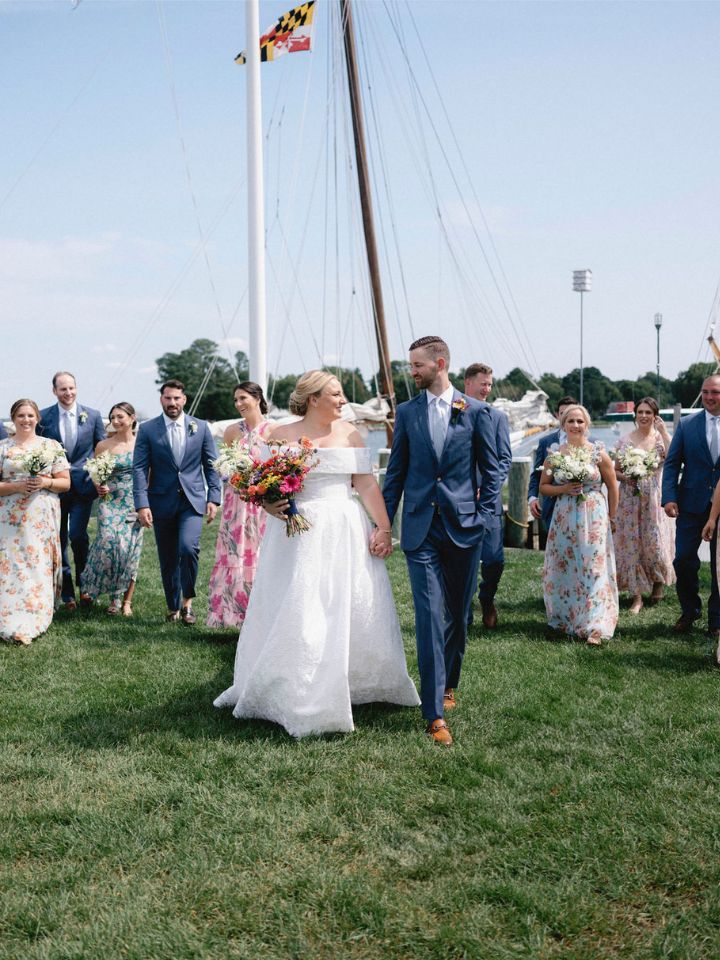 Bride and Groom lead their wedding party across a green grass lawn.