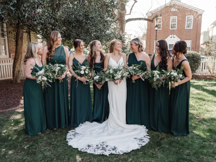 bridewithforestgreenbridesmaidsdresses Bride with her bridesmaids, all in a dark green dress, carrying white and neutral bouquets