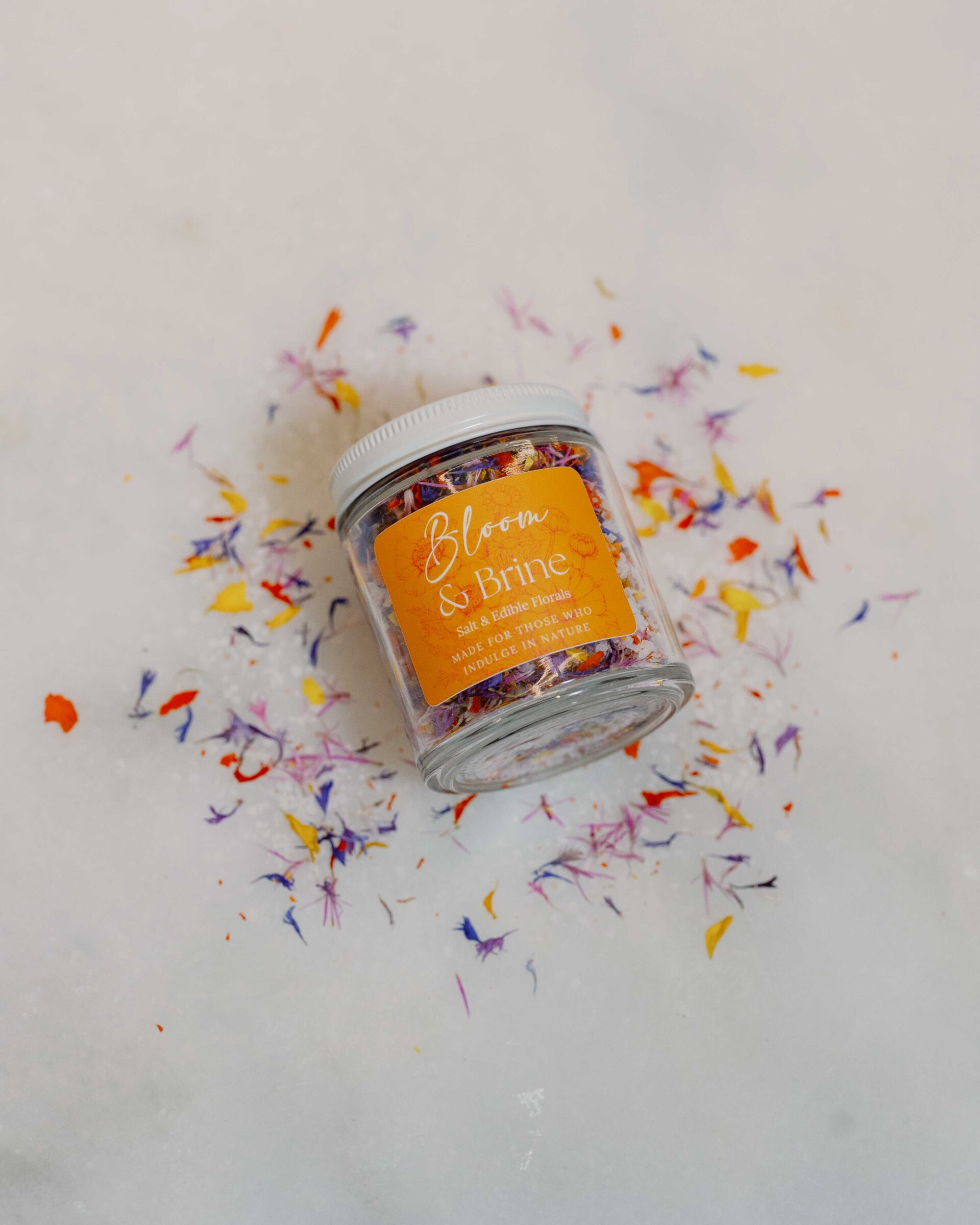 Jar of edible flower petals and salt on a white countertop.