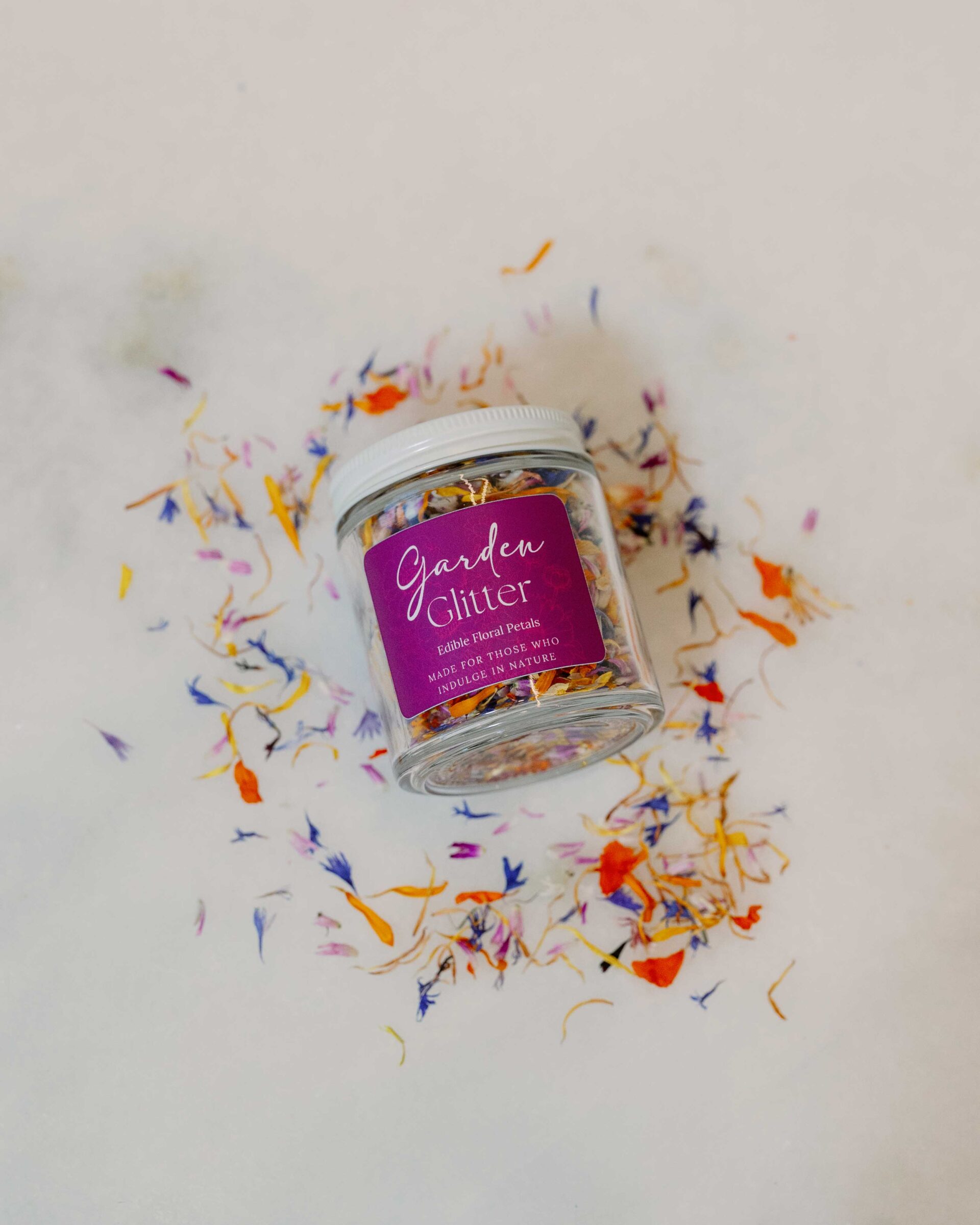 A jar of edible florals sits among loose petals.