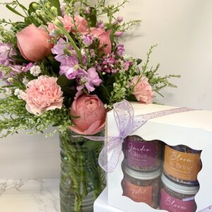A flower vase stands behind a gift set of four jars of edible florals.