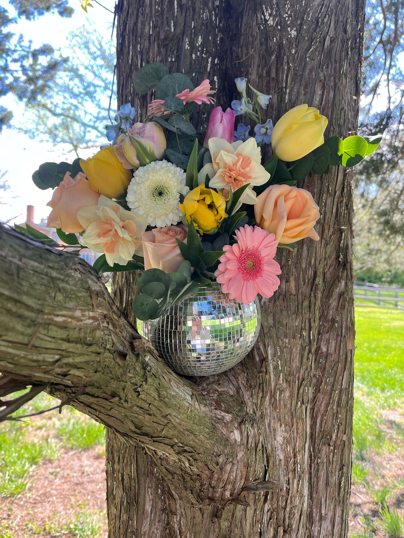 A spring colored florals disco ball arrangement in a tree.