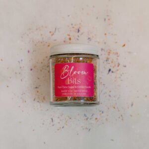 Jar of floral sugar on a counter surrounded by loose sugar and petals.