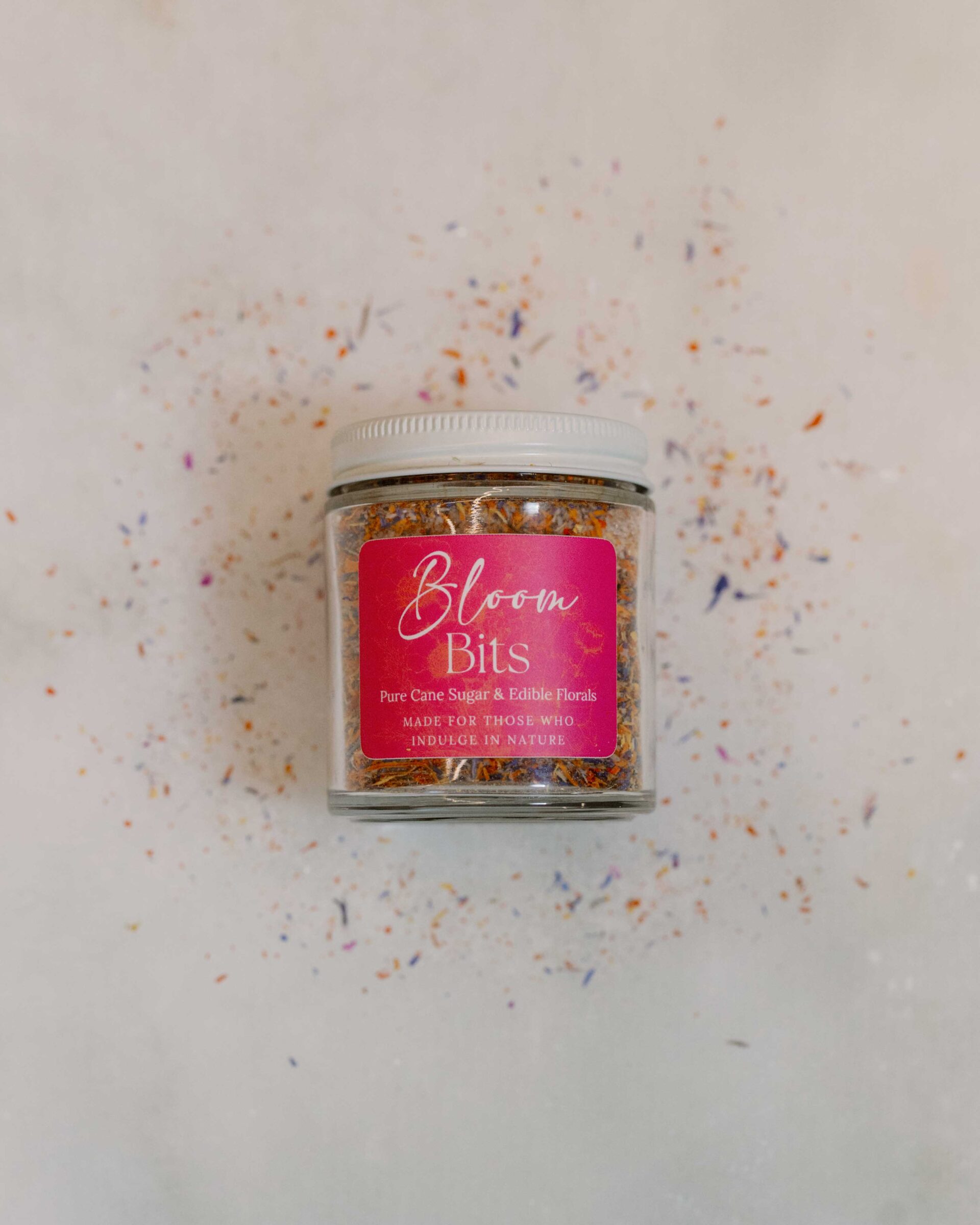 Jar of floral sugar on a counter surrounded by loose sugar and petals.