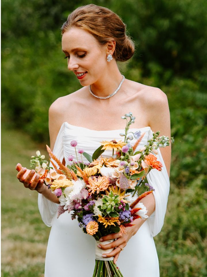 Bride smiles down at her flower bouquet full of garden style autumn flowers.
